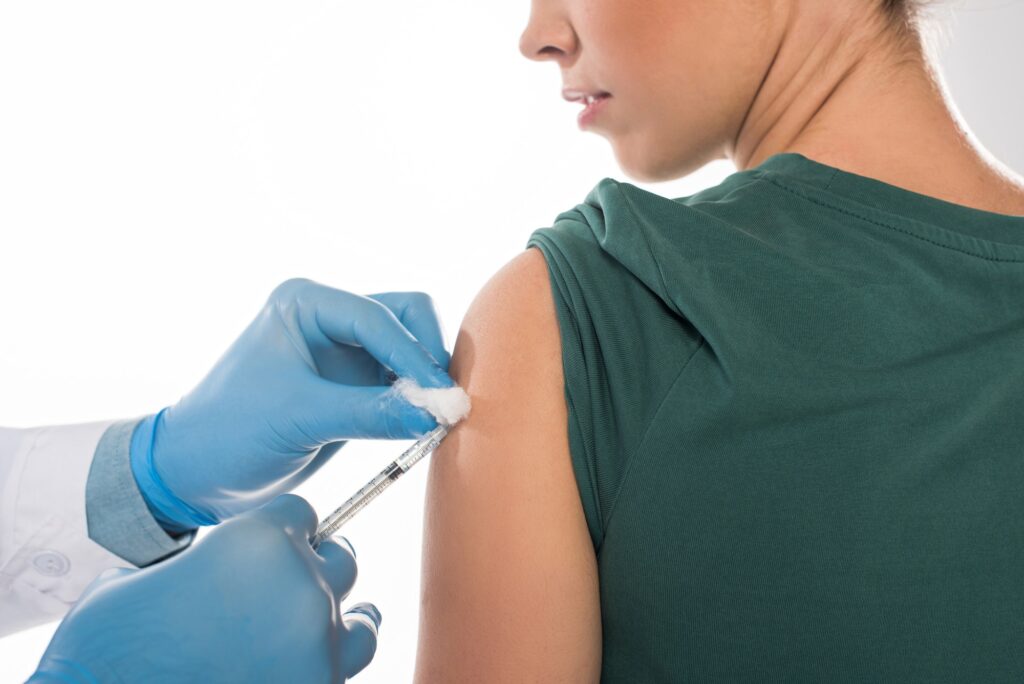 Cropped view of doctor with cotton wool and syringe doing vaccine injection to patient isolated on